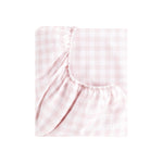 The Gooselings Pink Picnic Gingham Bedding is a folded fitted sheet with a light pink and white check pattern, featuring elastic edges. Made from pure materials and OEKO-TEX certified, it ensures breathable comfort for baby bedding.