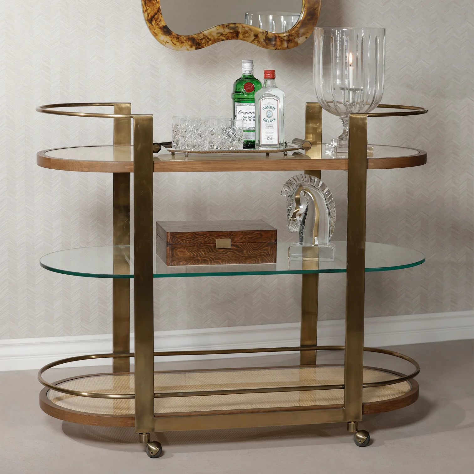 The Zodax Sloane Bar Cart, crafted with gold and glass, features space for liquor bottles, accessories, glasses, ice bucket, a decorative box, and a horse head sculpture—ideal for enhancing your home bar.