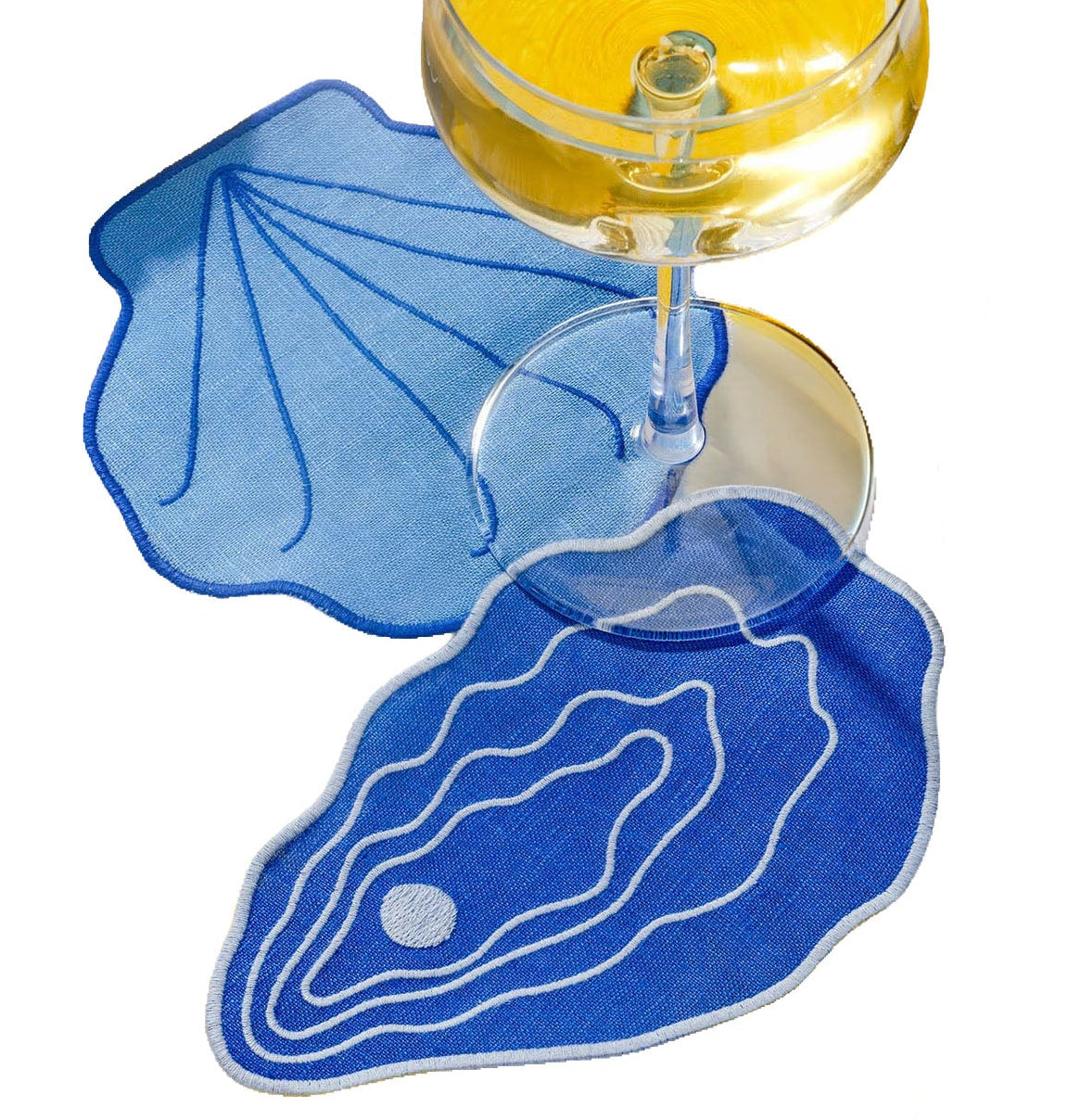 Two blue linen Shell Cocktail Napkins shaped like seashells under a stemmed glass of white wine.