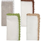 The Kim Seybert Shell Edge Napkin Set includes four linen napkins in neutral tones, each with a unique crocheted lace trim—white, brown, green, and beige—ideal for bohemian-inspired table settings.