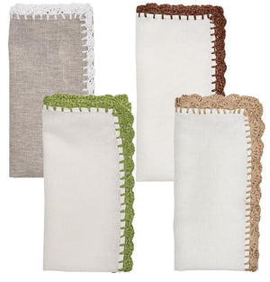 The Kim Seybert Shell Edge Napkin Set includes four linen napkins in neutral tones, each with a unique crocheted lace trim—white, brown, green, and beige—ideal for bohemian-inspired table settings.