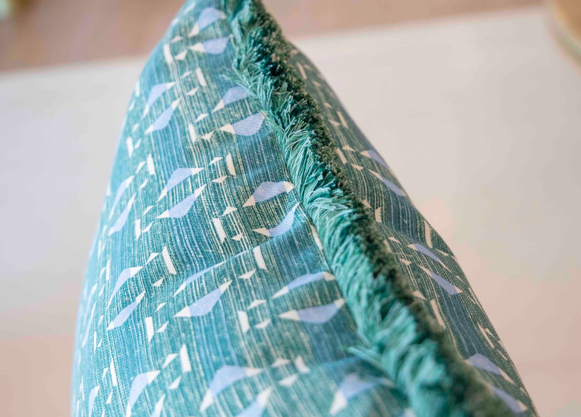 Close-up of the Associated Design Teal Sicily Outdoor Pillow, featuring a white bird pattern and green fringe trim, expertly crafted for a touch of luxury in your home.