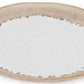 The Burlington Bluff Dinnerware Collection by Simon Pearce features a round ceramic plate with a beige rim, white center, and irregular edge design where the colors meet, inspired by pinch-pot styles.