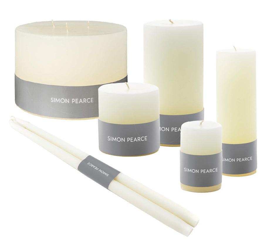 The Ivory Candle Collection by Simon Pearce features artisan candles in assorted shapes and sizes, each with a gray "Simon Pearce" label, adding small-batch elegance to any home.