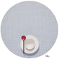 A white cup and saucer with a red spoon sit on a light blue Chilewich Round Placemat, made from phthalate-free Terrastrand yarns, with "Sky" labeled in the bottom right corner.
