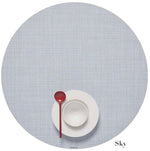 A white cup and saucer with a red spoon sit on a light blue Chilewich Round Placemat, made from phthalate-free Terrastrand yarns, with "Sky" labeled in the bottom right corner.