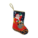 The Bauble Stockings "Sleigh Ride Santa" features a hand-stitched needlepoint Santa holding a green gift bag, adorned with stars and a hanging loop—ideal as festive décor or a unique Christmas ornament.