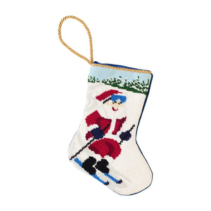 The Bauble Stockings Slopeside Santa Skiing Needle Point Stocking features a hand-stitched Santa skiing with a gold hanging loop and snowy background—perfect ski holiday decor for your mantel.