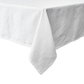 The Juliska Berry Scallop Tablecloth, in white linen and crafted in Portugal, features an elegant scallop trim and drapes gracefully over the corner of a rectangular table against a plain background.