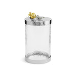 The Michael Aram Pomegranate Silver & Gold Canister features a clear cylindrical glass jar with a silver-toned hammered metal lid and a gold-silver pomegranate accent, inspired by ancient motifs from the Pomegranate Collection.