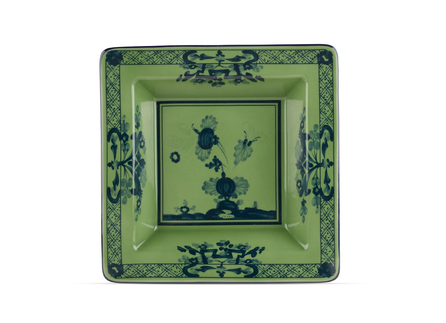 The Oriente Italiano Malachite Dinnerware Collection by Ginori 1735 features green ceramic plates inspired by Faenza ceramics, with dark blue floral and geometric borders and central floral motifs.