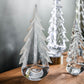 Three glass trees from the Simon Pearce Snowy Branches Evergreen Tree Collection are displayed on a wooden surface against a neutral background, inspired by Vermont winter woods.