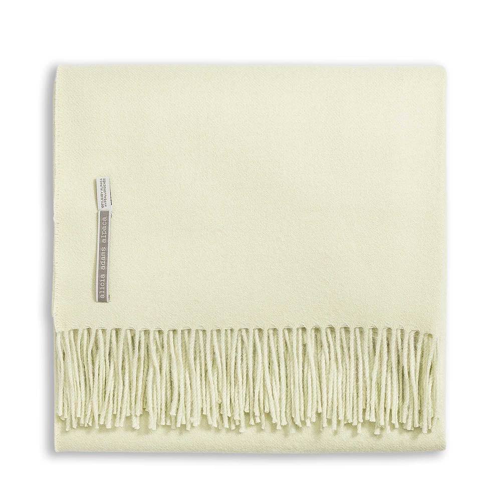 The Alicia Adams Alpaca Classic Throw Collection features a folded pale yellow baby alpaca blanket with fringe and a fabric label, fair-trade made in Peru—a soft, luxurious accent for any space.