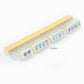 A long row of Oh My Mahjong Tile Collection soap bars, cream-colored and intricately designed like hand-painted Mahjong tiles, is displayed on a clear acrylic holder.