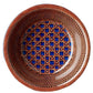 The Patagonia Blue Melamine Dinnerware Collection by Mario Luca Giusti features a round plate with a geometric lattice pattern in brown and blue, viewed from above against a white background—blending antique charm with modern style.