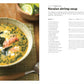 A bowl of Keralan shrimp soup, featured in The Soup Book from Penguin Random House, is garnished with shrimp and green herbs, and sits on a bamboo mat beside lime wedges and a spoon.