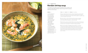 A bowl of Keralan shrimp soup, featured in The Soup Book from Penguin Random House, is garnished with shrimp and green herbs, and sits on a bamboo mat beside lime wedges and a spoon.