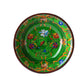 The Pancale Green Melamine Dinnerware Collection by Mario Luca Giusti features round plates with a green background, adorned with colorful floral and abstract patterns in the brand’s modern antique style.