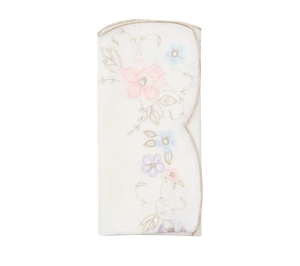 The Printemps Napkin Set by Kim Seybert features folded white napkins with embroidered pastel flowers and gold-trimmed scalloped edges, inspired by the brand’s signature floral designs.
