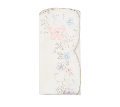 The Printemps Napkin Set by Kim Seybert features folded white napkins with embroidered pastel flowers and gold-trimmed scalloped edges, inspired by the brand’s signature floral designs.