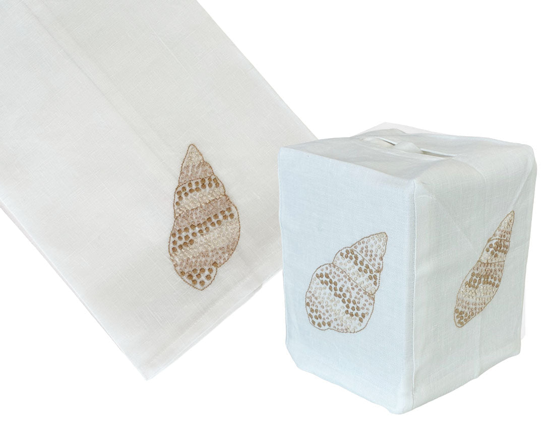 The Haute Home Speckled Conch Coaster & Bath Collection includes a premium white linen napkin and tissue box cover, each adorned with an embroidered brown seashell motif.