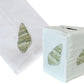Haute Home’s Speckled Conch Coaster & Bath Collection includes a white Italian linen tissue box cover and matching towel, both adorned with an embroidered green seashell motif.