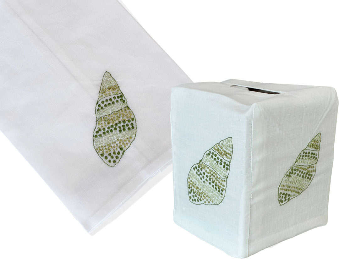 Haute Home’s Speckled Conch Coaster & Bath Collection includes a white Italian linen tissue box cover and matching towel, both adorned with an embroidered green seashell motif.