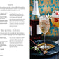 Two glasses of Spritz Cocktails garnished with fresh fruit and herbs sit on a table next to a bottle of rosé, with cocktail recipes from Simon & Schuster displayed on the left page.