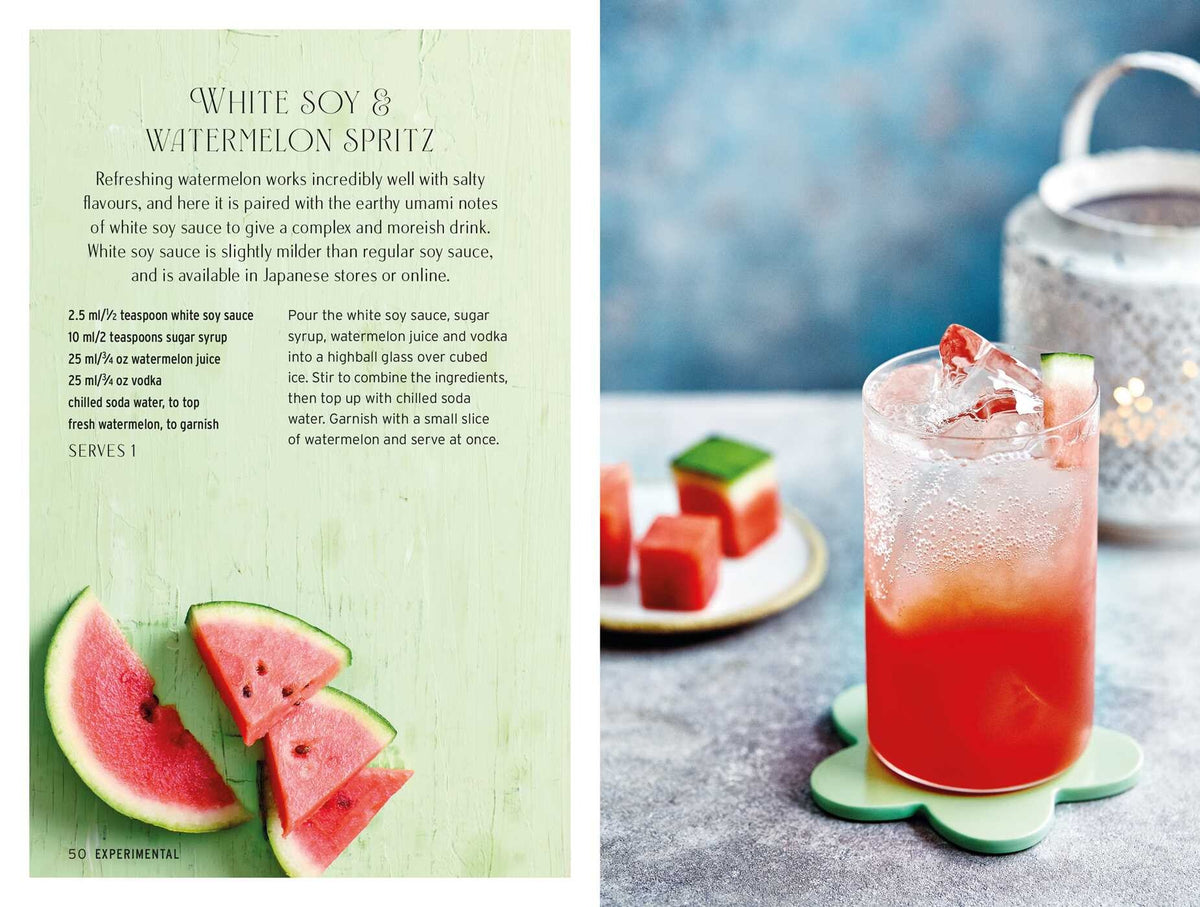 A glass of pink Spritz Cocktails by Simon & Schuster, served over ice with a touch of Italian amaro, rests on a green coaster beside a plate of fresh watermelon slices. In the background, a candle lantern casts a warm glow.