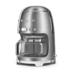 The SMEG Drip Filter Coffee Machine Collection by Smeg is a stainless steel coffee maker with a glass carafe, 10-cup capacity, and a digital display. The brand name "Smeg" is prominently visible on the front.