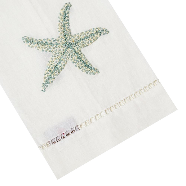 The Haute Home Starfish Bath Collection in Aqua features a white towel with a blue starfish design, hand-embroidered edges, and label. Inspired by Italian linen, it adds elegance to any space.