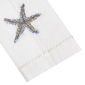 The 13 x 18" Starfish Tip Towel by Haute Home is crafted from white Italian linen, showcasing a hand-embroidered starfish in blue and gold.