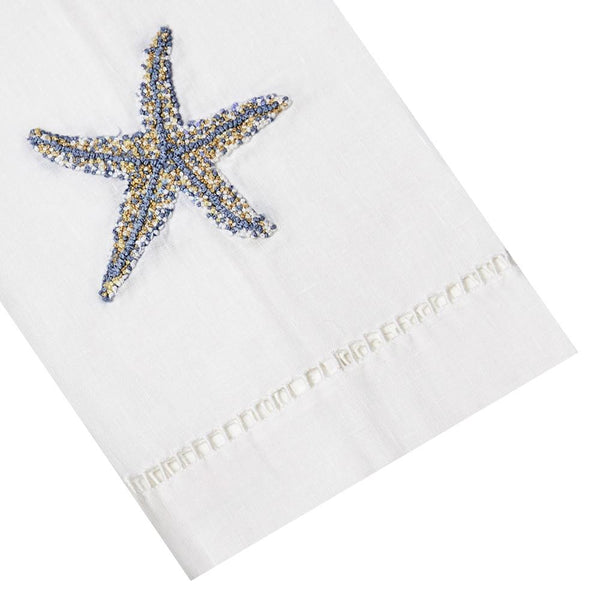 The 13 x 18" Starfish Tip Towel by Haute Home is crafted from white Italian linen, showcasing a hand-embroidered starfish in blue and gold.