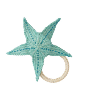 The Mercedes Salazar Starfish Napkin Ring gracefully features a woven blue starfish on a circular beige rattan ring, blending artisanal charm with coastal elegance against a white background.