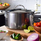 The Hestan NanoBond Covered Stockpot rests on a kitchen counter amid fresh tomatoes, limes, red onion, and jalapeños—ideal for crafting soups or delicious pasta dishes.