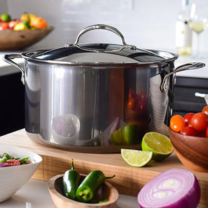 The Hestan NanoBond Covered Stockpot rests on a kitchen counter amid fresh tomatoes, limes, red onion, and jalapeños—ideal for crafting soups or delicious pasta dishes.