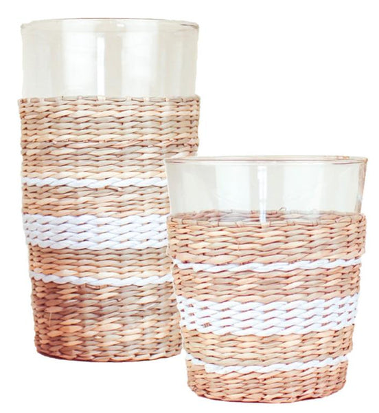 The Be Home Seagrass White Stripe Collection includes two clear glass holders wrapped in a seagrass design with white stripes, featuring one tall highball and one short wide tumbler.