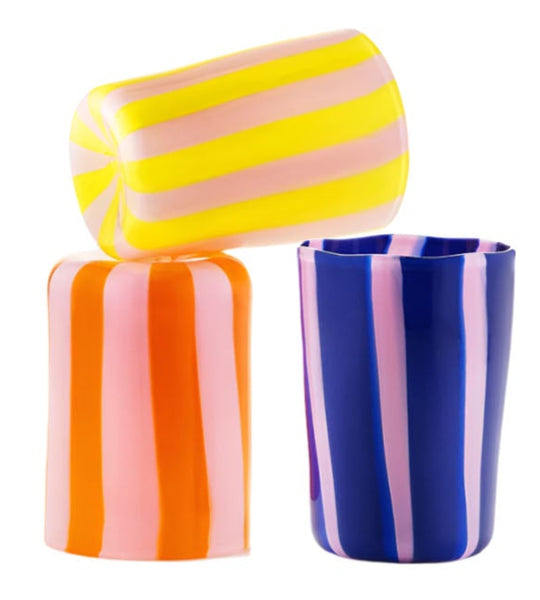 The Aquazzura Murano Dolcevita Stripe Tumbler Collection by Aquazzura Casa features three handblown Italian glass cups, vibrant in yellow and pink, orange and pink, and blue and pink stripes, highlighting the craftsmanship of Murano glass.