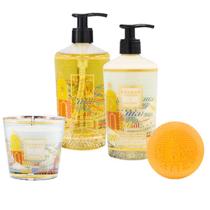 Baobab Collection Saint Tropez Body Wellness Collection: two pump bottles, a round orange soap, and a glass candle—all with vibrant patterned labels—bring fresh fragrance and style to your space.