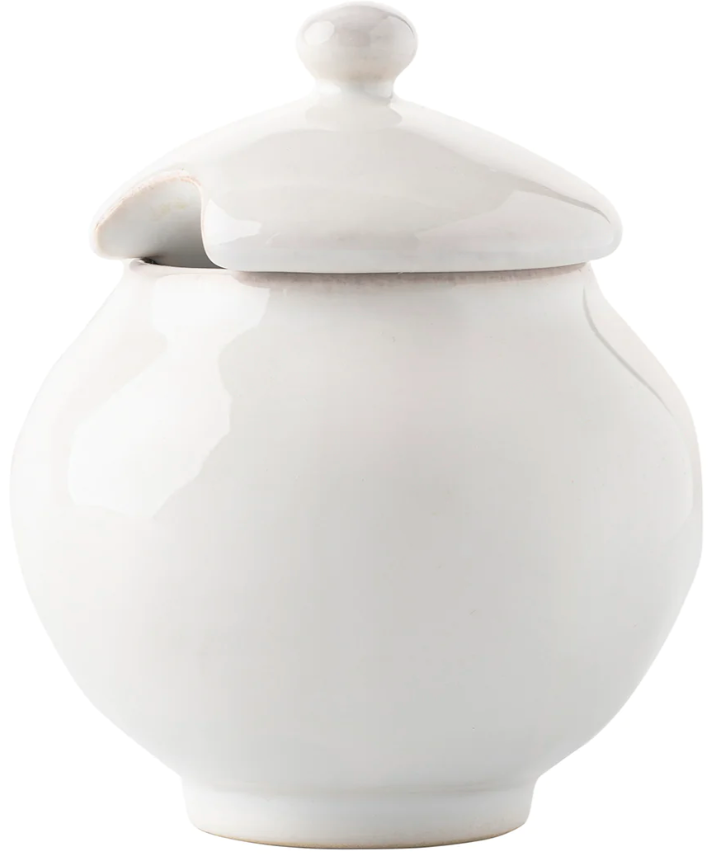 The Juliska Puro Whitewash Dinnerware Collection features a white ceramic sugar bowl with a rounded shape, lid, and spoon notch—ideal for teatime or enhancing a neutral table setting.