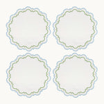 Four round white embroidered Sugus Table Linen Collection placemats with scalloped edges and blue and green decorative detailing.