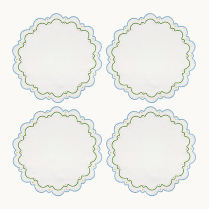 Four round white embroidered Sugus Table Linen Collection placemats with scalloped edges and blue and green decorative detailing.