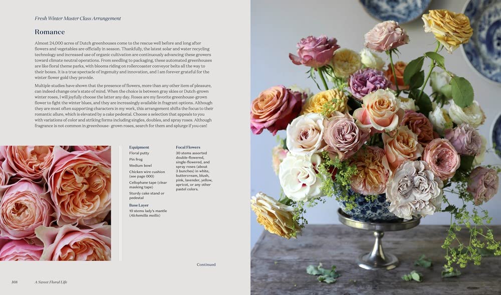 An exquisite arrangement from Penguin Random House’s “A Sweet Floral Life” showcases assorted roses in pink, peach, yellow, and cream hues displayed in a dark metal vase on a table, beautifully capturing the artistry found within expert floral designs, with softly blurred plates visible in the background.