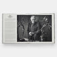 An open book reveals a black and white photo of a man with sculptures on a table, likely inspiring his next jewelry design. Text on the left page highlights the artistic legacy of creators like Sybil and David Yurman in fine jewelry. "Sybil and David Yurman: Artists and Jewelers" by Phaidon.