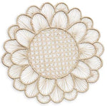 The Symi Rattan Placemat Collection by Themis Z features round, handcrafted placemats with a flower-like pattern, tightly woven center, and petal-shaped edges made from natural-colored fibers by Colombian artisans.