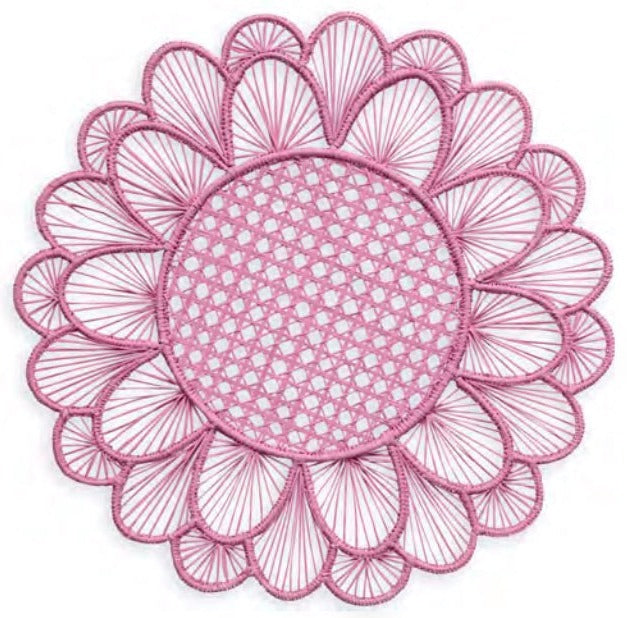 The Symi Rattan Placemat Collection by Themis Z features a round, pink placemat with a woven center and petal-shaped edges, handcrafted by Colombian artisans and shown on a white background.