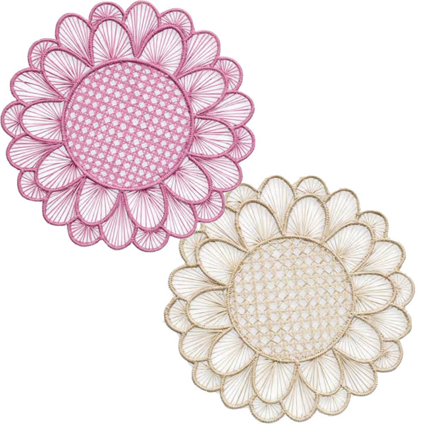 Themis Z offers the Symi Rattan Placemat Collection, featuring two handcrafted round placemats with scalloped edges by Colombian artisans. One showcases pink and white hues, the other beige and white, both with intricate radial patterns woven from palm fibers.