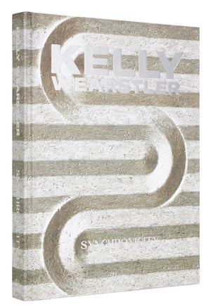 The image shows the cover of the Rizzoli book "Kelly Wearstler: Synchronicity," featuring an abstract design with parallel lines and curves in neutral tones. The title and author's name are displayed in large metallic text, reflecting her renowned expertise in both residential and hospitality designs.