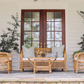 A porch featuring the Varnish Collection's Julianna Sofa, two artisan wicker chairs, and a glass-top coffee table, set by double wooden doors and flanked with two potted plants crafted from natural materials.