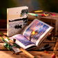 Fishing The Ultimate Book by Graphic Image is open on a wooden table, featuring a fish photo, with fishing rods, reels, lures, and tackle arranged around it.